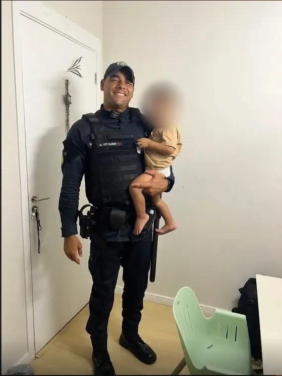 José Kleber, uniformizado e sorrindo, com o filho no colo