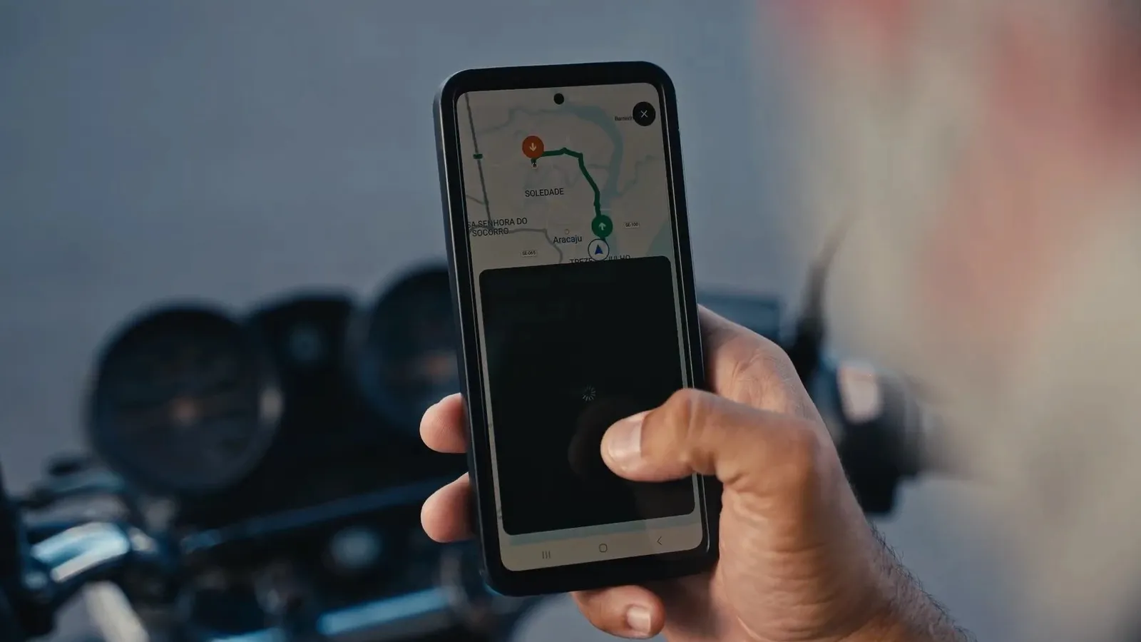 Celular com o mapa de um aplicativo de carona em Aracaju, ao lado do guidão de uma moto