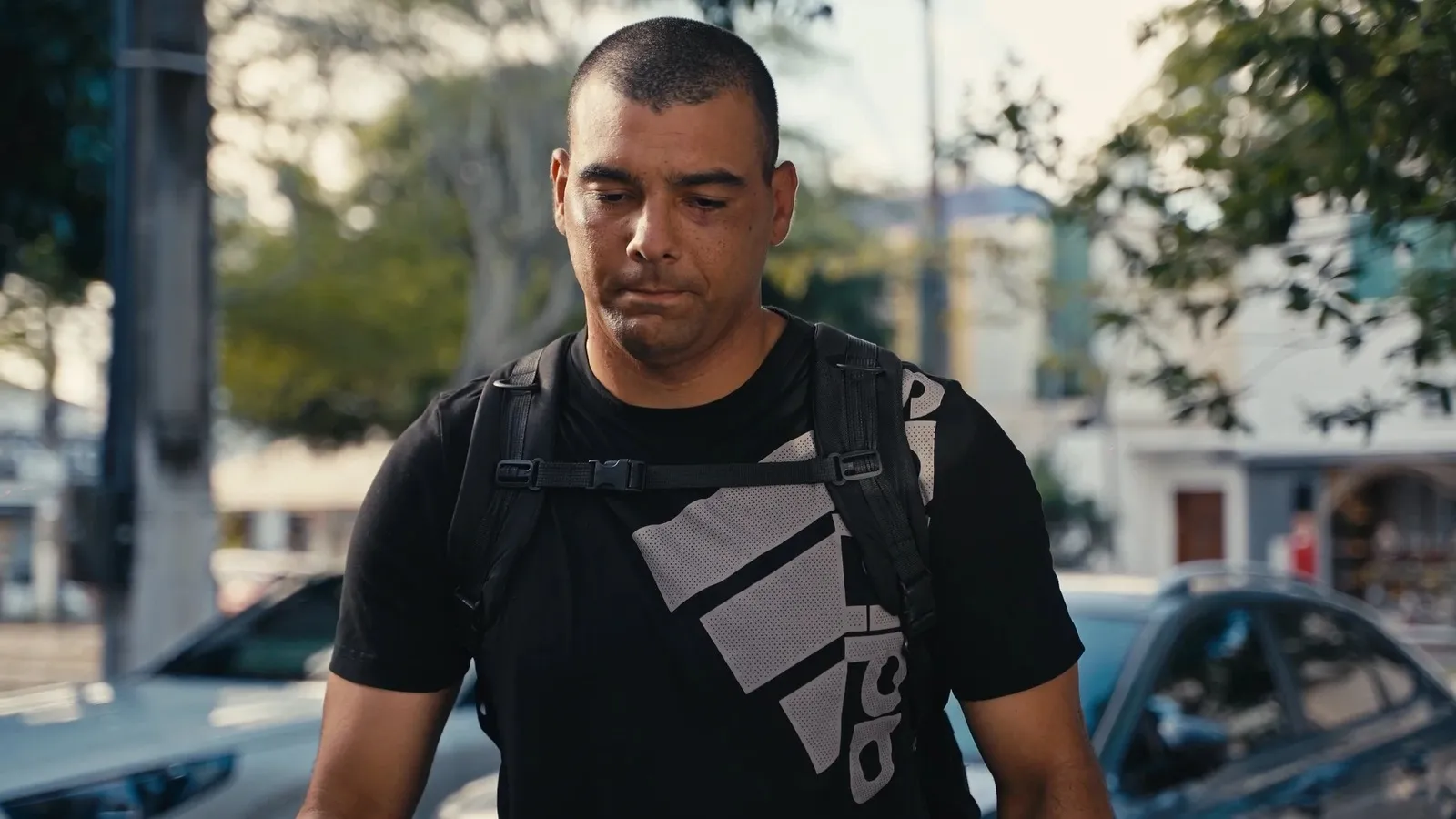 José Kleber caminhando na rua com mochila nas costas e expressão séria