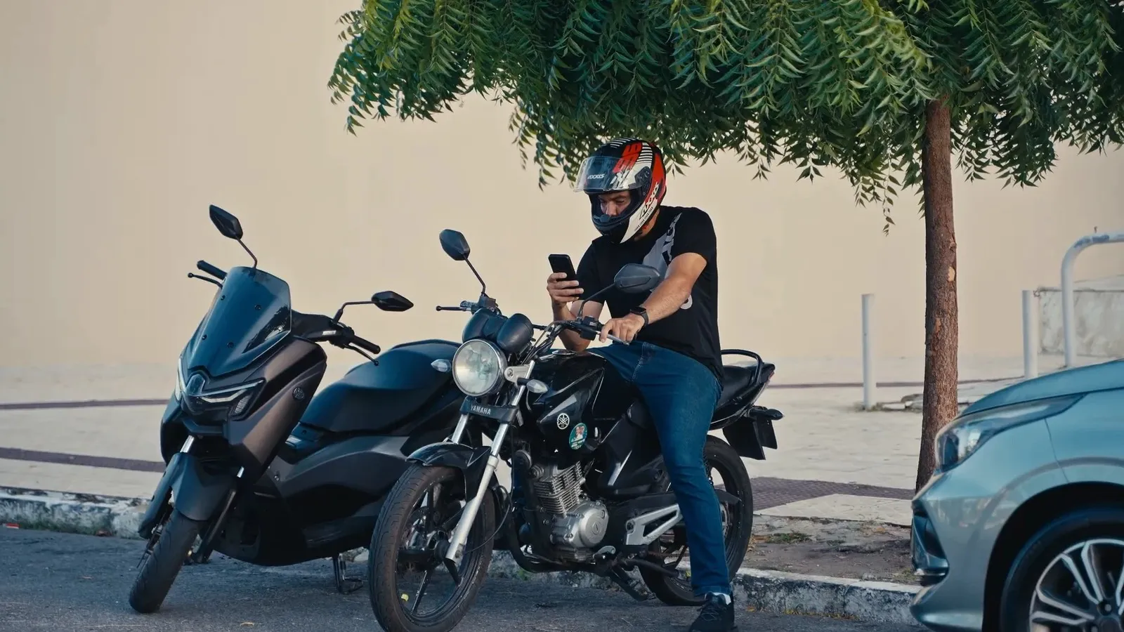 José Kleber de capacete, sentado em uma moto, olhando o celular
