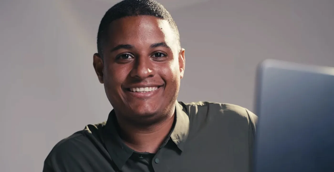 Raphael Martins sorrindo para a câmera, de camisa verde, ao lado de um notebook